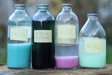 Colored insoluble compounds of silicates: copper, cobalt, nickel and dark blue iron pigment in glass bottles with chemical formulas.