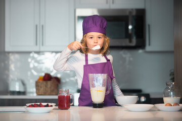 Child 7-8 years old in chef hat and apron. Chef child in apron and chef hat cooking at kitchen. Healthy food.