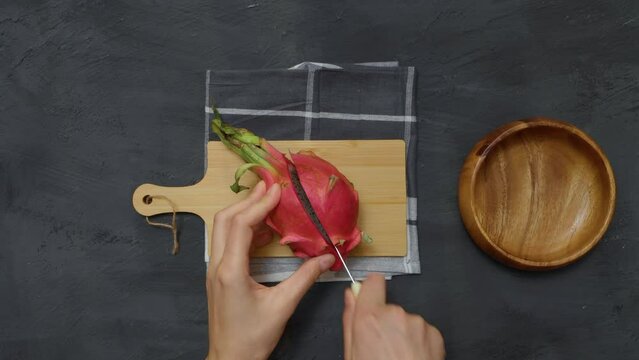 Hands cutting a pitahaya fruit a wooden board. Flat lay