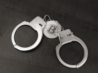 Cryptocurrency and crimes concept. Handcuffs on bitcoin coin on table. 