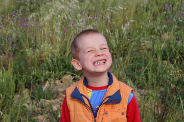 The blond short-haired boy smiles and shows crooked teeth. Cheerful six year old boy.