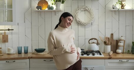 Pregnant Caucasian woman in kitchen, dancing with pure joy. Beaming smile on face, graceful movements express happiness. Tenderly caressing baby bump, showering it with love and affection.