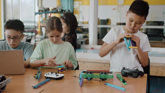 Children in a class at a robotics lesson sitting at the table and assembling different modules with high concentration. Concept of technological modern education
