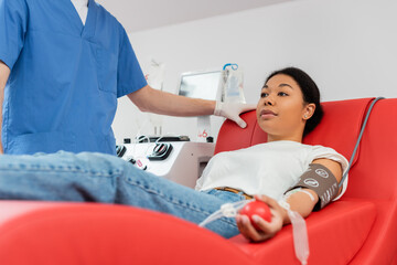 doctor in blue uniform standing near multiracial woman sitting on comfortable medical chair near...