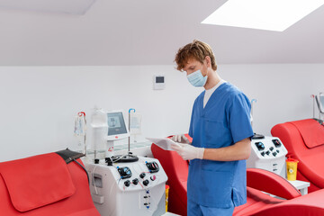 redhead doctor in blue uniform, medical mask and latex gloves looking at digital tablet near...
