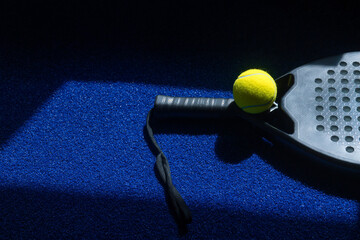 Black professional paddle tennis racket and ball with natural lighting on blue background....
