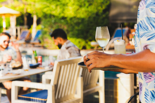 Waiter serving glass of white wine and cocktail to customer.