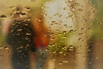 Abstraktes Motiv von jungem Paar auf Straße hinter Glasscheibe mit Regentropfenmuster und Licht bei Regen am Morgen im Frühling