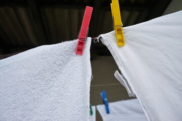 Weiße Handtücher mit bunten Wäscheklammern hängen an Leine zum Trocknen bei Sonne am Mittag im...