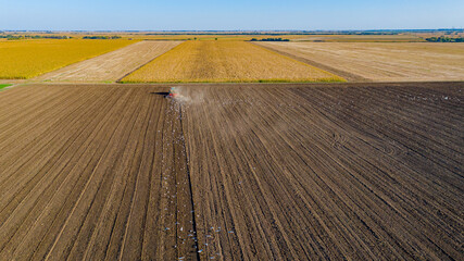 Aerial shot of agricultural field with tractor pulling a disc harrow over agricultural field,...