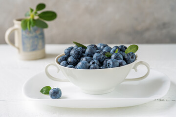 Fresh blueberries in a white teacup on the white wooden table with grey concrete background,...