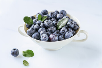 Fresh blueberries in a white teacup on the white background, closeup, top view
