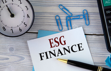 ESG finance - words on a white sheet on the background of a calculator, alarm clock and pen