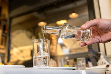 Greek tsipouro being poured into a glass with ice cubes at a taverna. Soft focus
