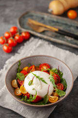 Salad with traditional italian buratta cheese with cherry tomatoes  and arugula leaves in bowl on the table