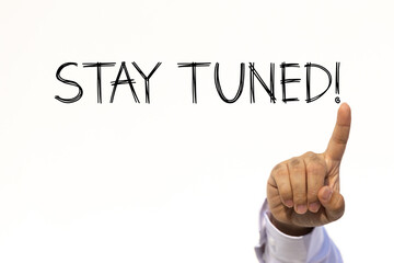 Stay tuned text on white wall background with businessman's finger point at the message with empty space. This message can be used as business concept about stay tuned.