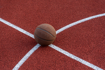 Basketball ball on the ground. Close-up ball on the red court. Basketball on the street or indoor court. Sports gear without people. Minimalism. Template, sport background	