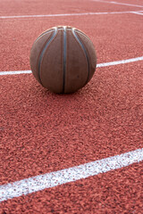 Basketball ball on the ground. Close-up ball on the red court. Basketball on the street or indoor court. Sports gear without people. Minimalism. Template, sport background	