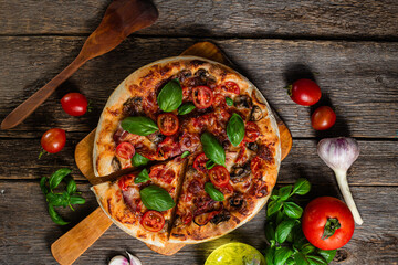 Appetizing pizza. Pizza with ham, mushrooms and tomatoes on a wooden background