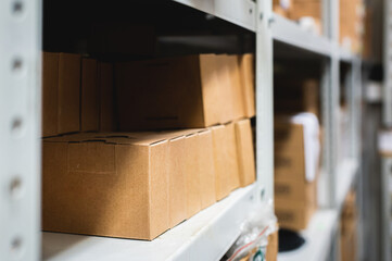 Rows of shelves with cardboard boxes in a modern warehouse, close-up. Brown boxes on metal shelving, side view, background blurred