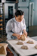 Fototapeta na wymiar concentrated beautiful woman baker lays out raw bread rolls from molds before baking bakery production of pastries