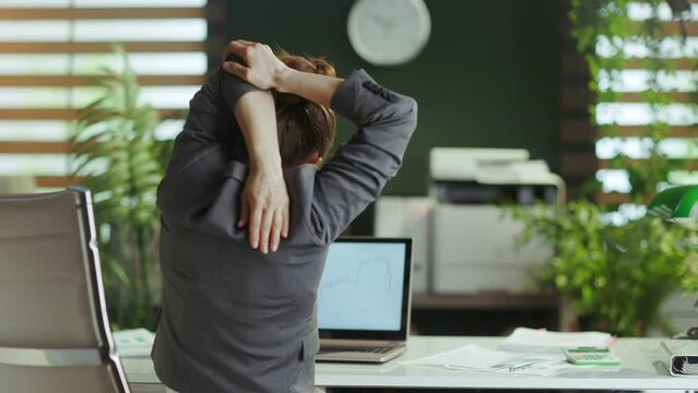 Sustainable workplace. Seen from behind modern business woman in a grey business suit in modern green office stretching hand.