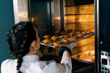 attractive baker takes ready buns and croissants from professional oven bakery production fresh...