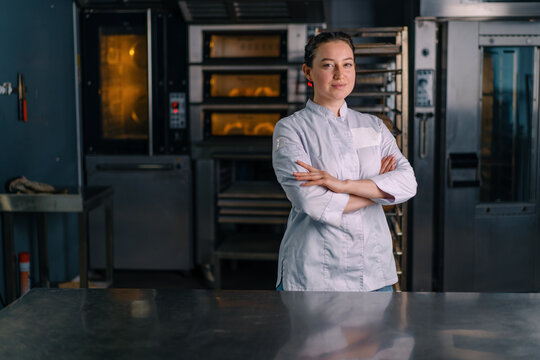 smiling beautiful woman baker in uniform stands near the oven before the start of work bakery production of pastries