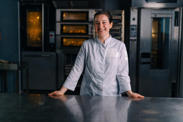 smiling beautiful woman baker in uniform stands near the oven before the start of work bakery...