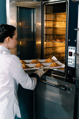 attractive baker takes ready buns and croissants from professional oven bakery production fresh...