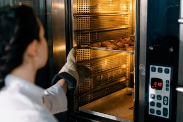 Foto op Plexiglas attractive baker takes ready buns and croissants from professional oven bakery production fresh baked goods © Guys Who Shoot
