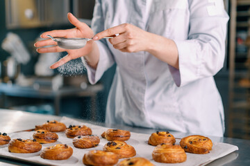 Obraz na płótnie Canvas attractive baker sprinkles powdered sugar on ready freshly baked hot fragrant buns baking production bakery
