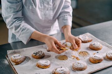 Obraz na płótnie Canvas beautiful woman baker tears ready freshly baked hot aromatic buns and checks dough bakery production