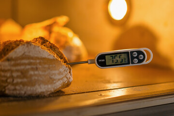 baker measures the temperature of freshly baked bread in the oven with a thermometer bakery production of pastries - obrazy, fototapety, plakaty