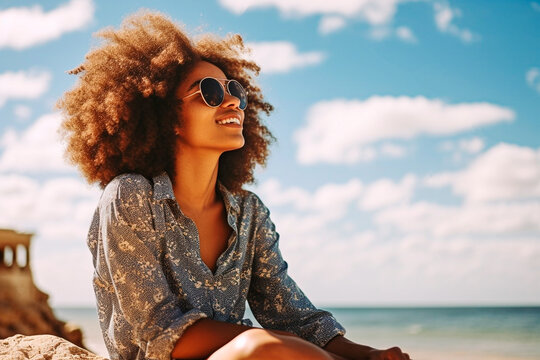 Young girl with afro hair sitting on the beach looking at the ocean