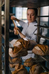 Foto op Plexiglas female baker takes out freshly baked fresh bread from the oven and puts it on the shelf in the kitchen of the bakery Culinary profession © Guys Who Shoot