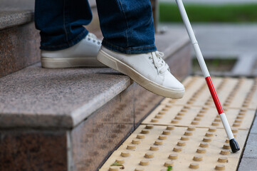 Close-up of female foot, walking stick and tactile tiles. Blind woman walking down stairs using a...