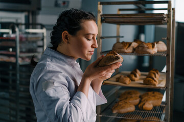 attractive female baker takes freshly baked fragrant bread from the shelf sniffs it checks its...