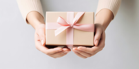 A woman's hands hold a craft gift box with pink  satin ribbon bow. Isolated on pastel grey background, with copy space, template for sale, promotion and gift banner. Generative AI photo imitation