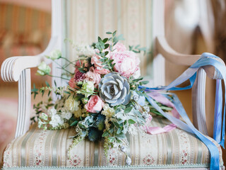 A bride's bouquet with echeveria, peonies, roses, eustoma lies on a vintage armchair. Blue, blue and pink ribbons on the bouquet. Wedding day.