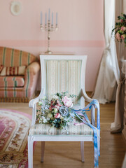 A bride's bouquet with echeveria, peonies, roses, eustoma lies on a vintage armchair. Blue, blue and pink ribbons on the bouquet. Wedding day. French-style room in pink tones.