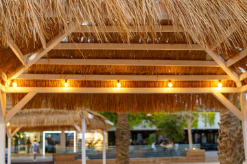 Straw beach umbrella canopy with evening lights and blurred city background. Thatched patio umbrella.