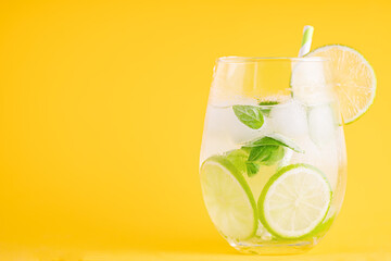 Summer lemonade with basil and lime on yellow background. One fresh summer cocktail with basil,...