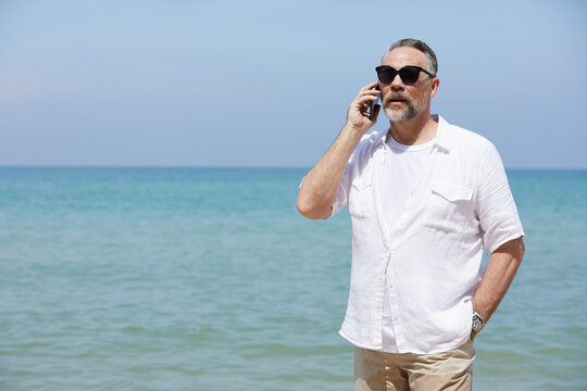 senior man talking by smartphone on the beach