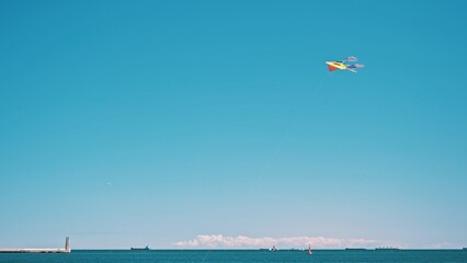 Fototapeta na wymiar Colorful Tethered Kite Floating in Air Flying in Strong Wind by Seaside