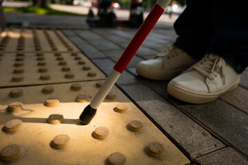 A close-up of a woman's feet with a tactile cane and a tactile tile indicating an obstacle.