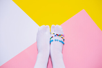 Two feet in white tabi socks wrapped with colored bead necklaces on a pink, white and yellow...