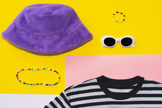 Round white plastic sunglasses, fluffy purple panama, colorful necklace and a striped T-shirt. Fashion flat lay set