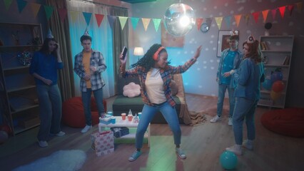 A group of friends are dancing in a room decorated with a party. An African American girl in red...