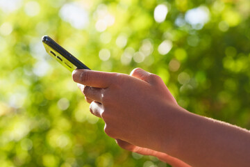 Close up of Black woman's hands using mobile phone, texting in nature leaf bokeh